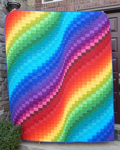 a multicolored quilt is displayed in front of a brick building