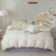 a bed with white sheets and purple comforter next to a lamp on the floor