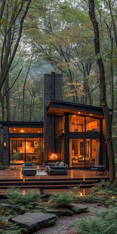 a modern cabin in the woods with lights on it's windows and patio area