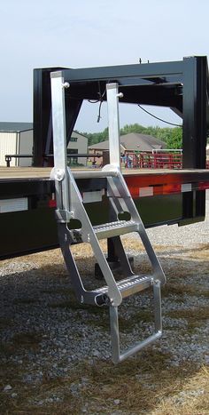 there is a ladder attached to the back of a large truck that's parked on gravel