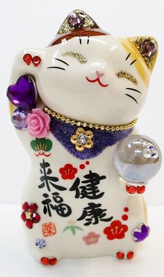 a white cat figurine with purple and pink flowers on it's chest