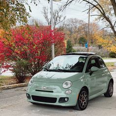 a small green car parked on the side of the road in front of some trees