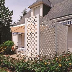 a house with a white lattice fence and flowers in the foreground, on a sunny day