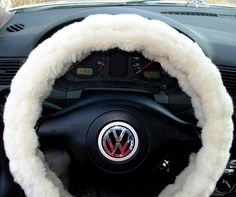 the steering wheel cover is covered with white fur and has a red vw emblem on it