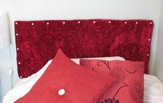 two red pillows sitting on top of a bed next to a white night stand and lamp