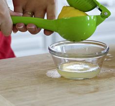 a person using a green spoon to mix something in a glass bowl on a wooden table