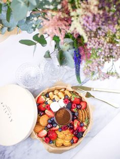 a platter filled with fruit and crackers on top of a marble table next to flowers