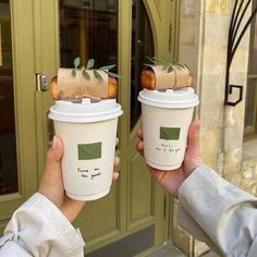 two people holding up coffee cups in front of a door with green leaves on them