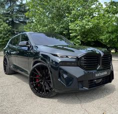 the front end of a black suv parked in a parking lot with trees behind it