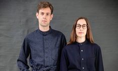 two people standing next to each other in front of a gray background wearing black glasses