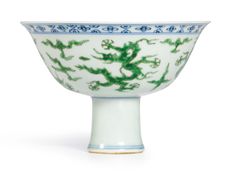 a green and white bowl with dragon designs on it's rim, sitting on a white surface