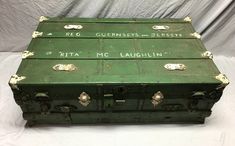 an old green trunk with writing on the lid and handles sitting on a white surface