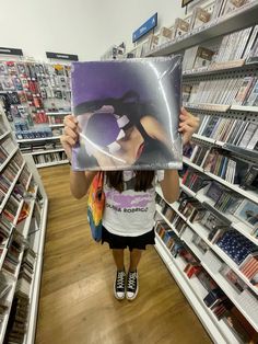 a woman holding up a poster in a store aisle with bookshelves behind her