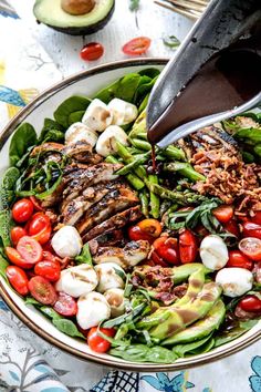 a bowl filled with salad and dressing being drizzled on top of it