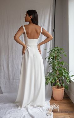 the back of a woman in a white dress standing next to a potted plant