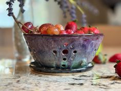 a bowl filled with lots of fruit sitting on top of a counter next to a vase