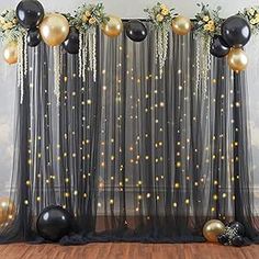 black and gold balloons are hanging from the back of a sheer tulle backdrop with flowers