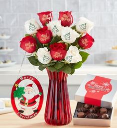 a red vase filled with white and red roses next to a christmas ornament