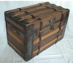 an old wooden trunk is sitting on a white sheeted surface with leather straps around it