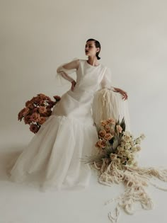 a woman in a white dress sitting next to flowers