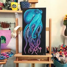 an octopus painting on a easel in front of a shelf with other art supplies