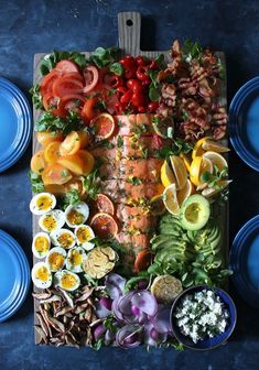 an assortment of food is laid out on a cutting board with blue plates and utensils