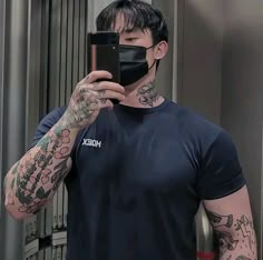 a tattooed man taking a selfie in front of a mirror with his cell phone