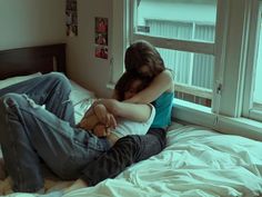 two people are sitting on a bed with their arms around each other as they hug