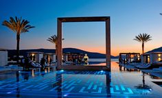 an outdoor swimming pool with lounge chairs and palm trees in the background at night time