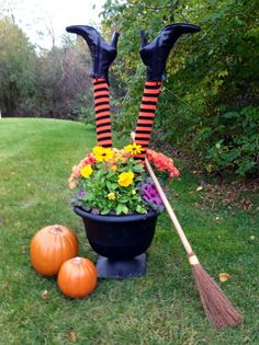 two halloween decorations are placed in a pot with flowers and brooms on the grass