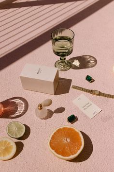 slices of citrus interspersed throughout luxury items like a perfume bottle, gold watch, vintage green wine glasse, and other jewelry items, all against a pink concrete background. Editorial Flatlay, Product Photography Flat Lay, Beauty Brand Photography, Jewellery Flat Lay, Desert Product Shoot, Desert Product Photography, Spring Product Photoshoot, Flat Lay Product Photography