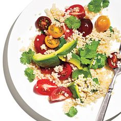 a white plate topped with tomatoes, cucumbers and couscouse next to a fork