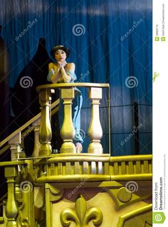 a statue of a woman on top of a yellow balcony with blue curtains in the background