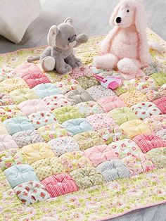 two stuffed animals sitting on top of a quilted baby bedding with pink and green accents