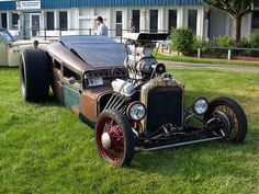 an antique car is parked on the grass in front of a building with people standing around it