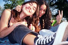 two young women sitting on the ground with their fingers in the air and one is holding up her peace sign