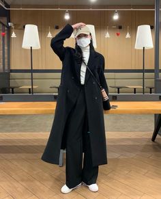 a person wearing a mask and coat standing in front of a long table with lamps