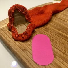 a wooden cutting board topped with a cut out piece of cloth and a pink paper