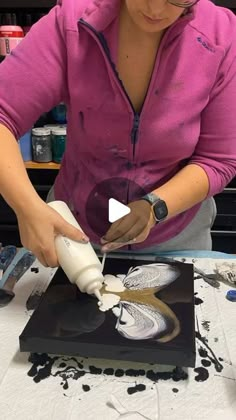 a woman is working on an art project with white paint and black paper, while she holds a pair of scissors