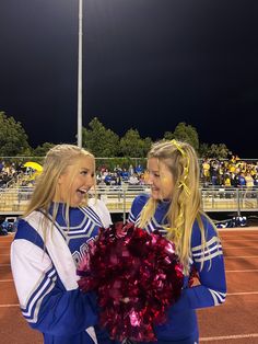 two girls in cheerleader uniforms holding a pom - pom at a football game