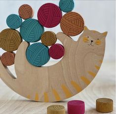 a wooden cat with balls of yarn on it's back sitting next to some wood pegs