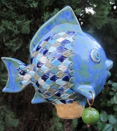 a blue fish statue sitting on top of a wooden pole next to some green plants