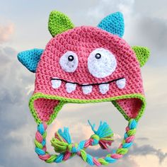 a crocheted hat with eyes and teeth hanging from a string in the sky