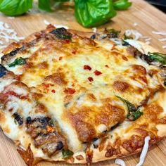 a pizza sitting on top of a cutting board covered in cheese and toppings next to basil leaves