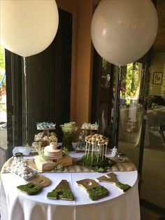 a table topped with cake and desserts next to two white balloons in the air