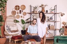 a man and woman sitting in a living room with plants on the wall behind them