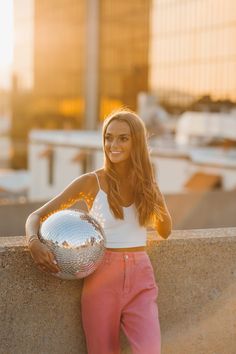 a woman leaning against a wall holding a disco ball