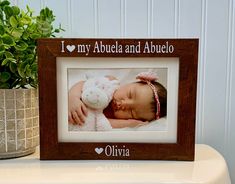 a wooden frame with a baby holding a stuffed animal in it's lap and the words, i love my abuella and abuelo