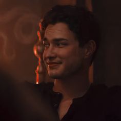 a young man is smiling and talking to someone in the dark with his hand on his hip