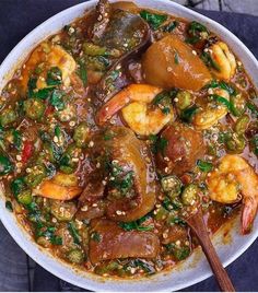 a white bowl filled with shrimp and vegetable stew next to a wooden spoon on top of a table